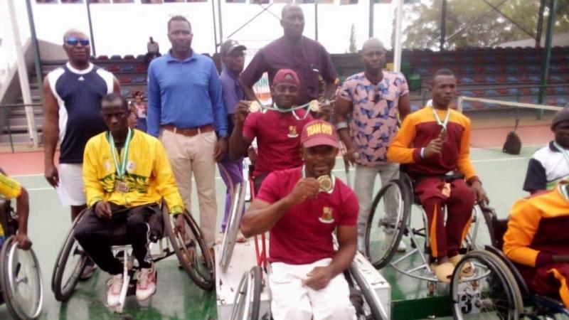 A group of wheelchair tennis players with medals on the podium and next to it.