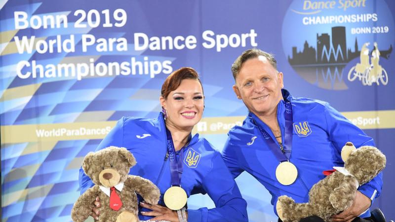 Image of a male and a female dancer in their wheelchairs and with their gold medals