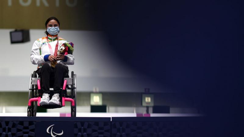 Avani Lekhara sits in her wheelchair on the Tokyo 2020 podium with a gold medal around her neck.