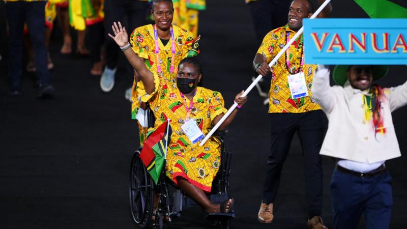 A woman in traditional clothes and in a wheelchair carries the Vanuatu flag in an athlete's parade.