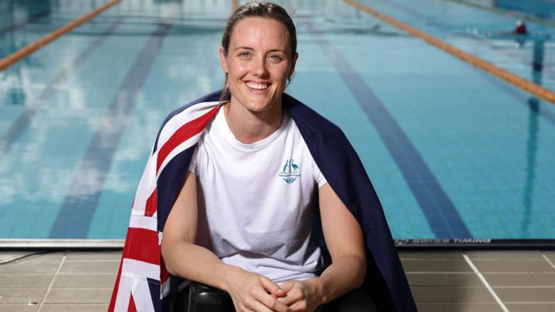 A woman with the Australian flag on her shoulders and a swimming pool in the background