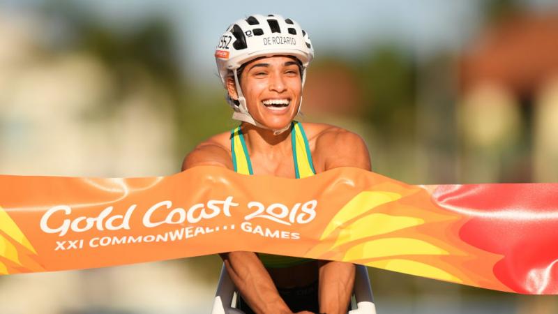 A female wheelchair racer crossing a finish line and smiling