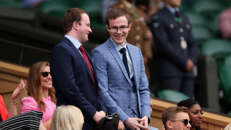 Two young men stand and smile as people around them sit and clap.