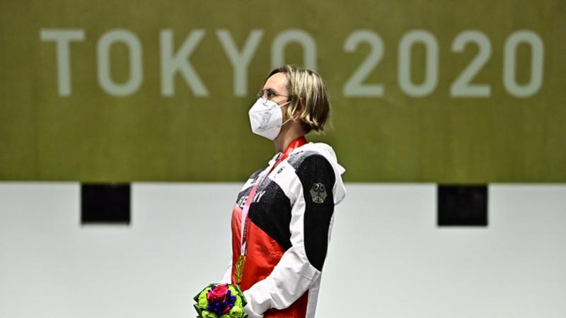 Image of a female Para shooter after winning gold, looking at the German national flag on the podium