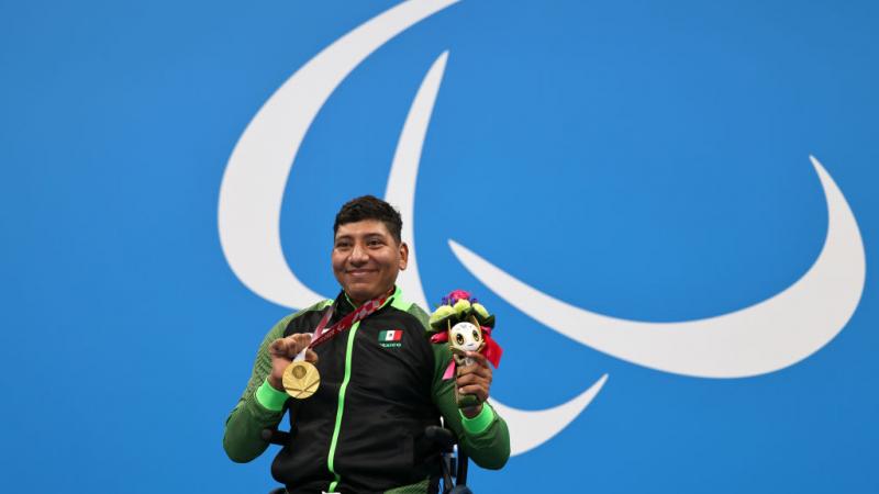 Image of a male Para swimmer in the podium with his gold medal and his flowers