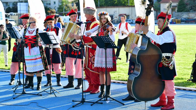 A group of musicians in traditional Polish clothing play on the athletics track in Cracow.