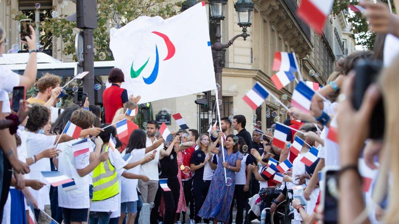 Many people wave the French flag to welcome a woman carrying the Paralympic flag