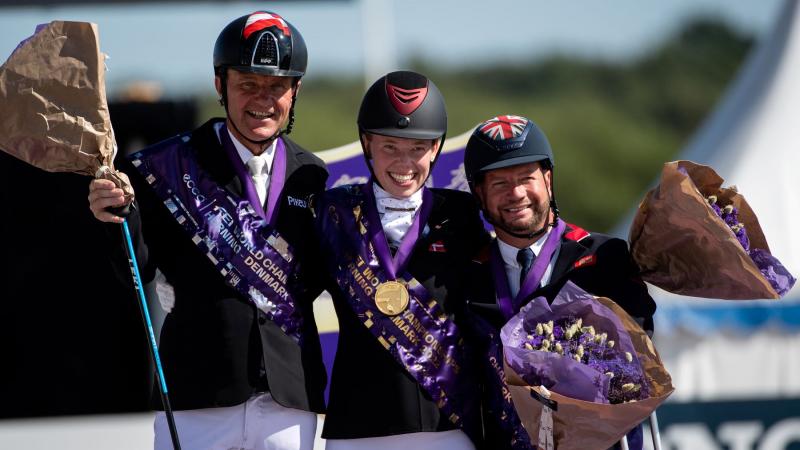 Three athletes smile after receiving their medals at the Para Dressage World Championships.