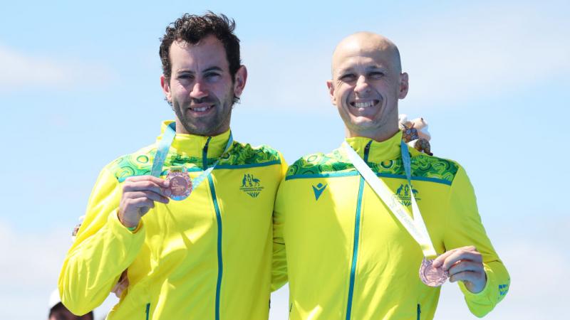 Para triathlete and his guide each hold a bronze medal and smile