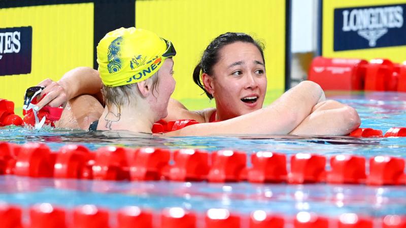 A female swimmer embracing another female swimmer looking surprised in the pool