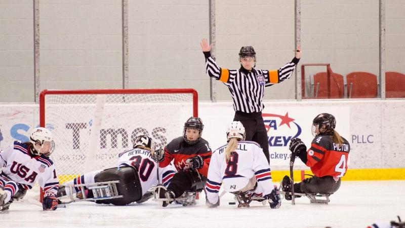 A female Para ice hockey official raising her arms in front of five female players