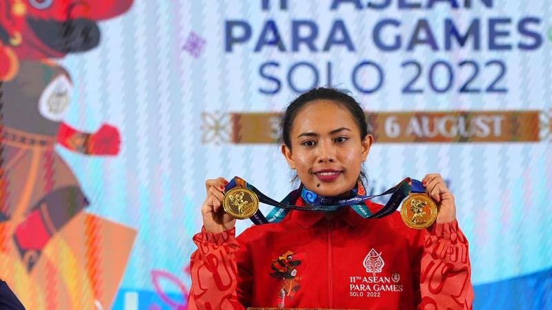 A woman showing her gold medals with a backdrop of the 11th ASEAN Para Games