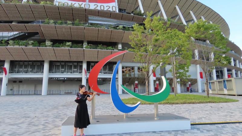 A former Paralympian poses with a violin in front of the Agitos symbol at the Olympic Stadium in Tokyo.