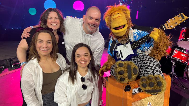 Two swimmers, a coach and manager pose with a puppet from the fictional band The Weirdos.