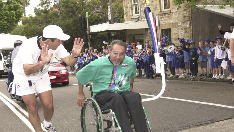 A man pushes his wheelchair in front of a crowd of young spectators as part of the Sydney 2000 torch relay.