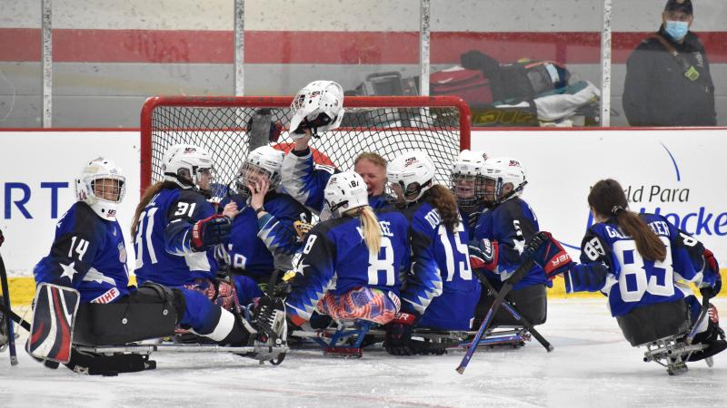 Female Para ice hockey players on sleds celebrate in a circle.