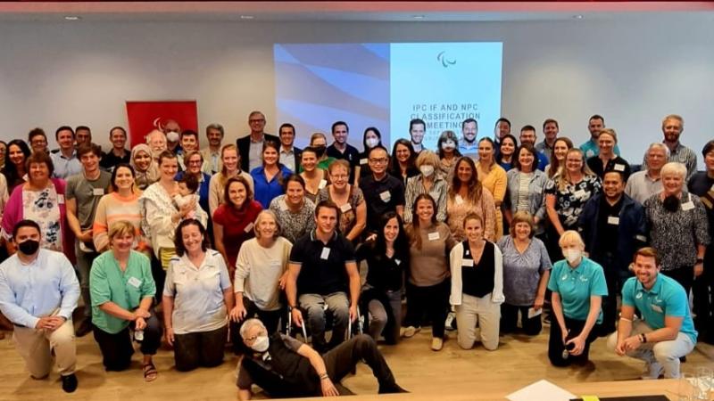 More than 70 people pose for a group photo in front of a screen that says "IPC IF and NPC Classification Meeting"