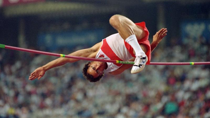 A male athlete jumps over the bar in a stadium full of spectators.