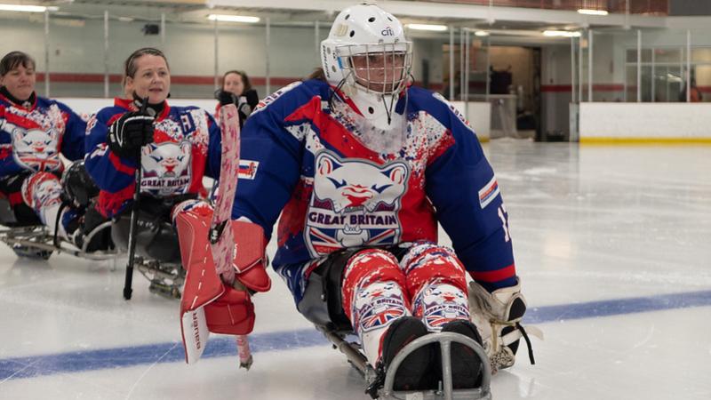 Female Para ice hockey players wearing Great Britain jerseys form a line on the rink.