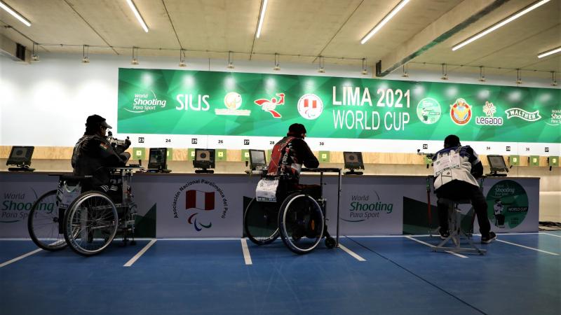 Three shooters in wheelchairs competing in an indoor shooting range