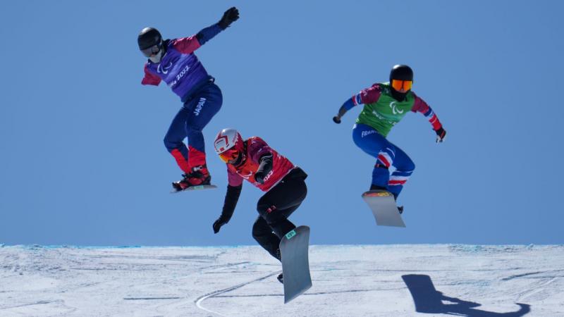 Three male Para snowboarders jump during the snowboard cross race at Beijing 2022.