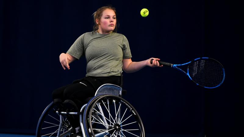 A female wheelchair athlete plays a forehand on a blue court.