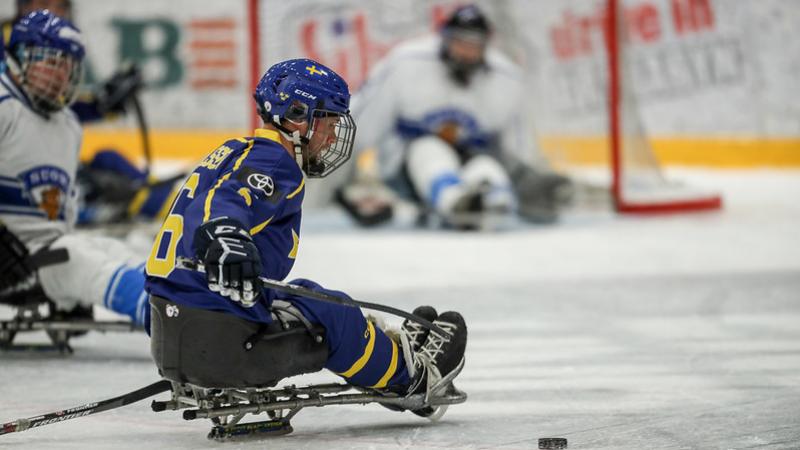 A Para hockey player preparing to shoot in front of an opponent with a goaltender in the background