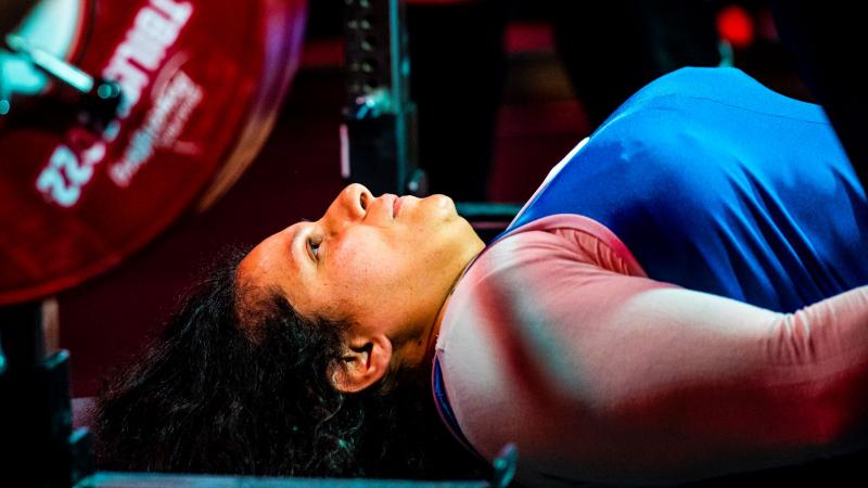 A female powerlifter lies on the bench and looks up at the bar.