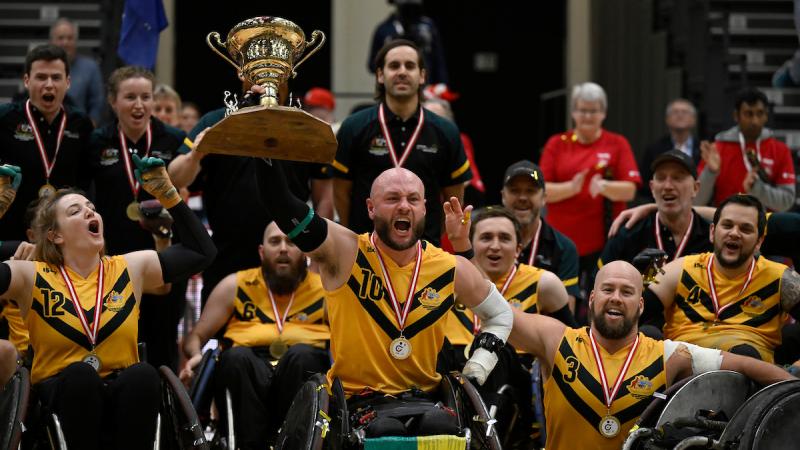 Wheelchair rugby players wearing yellow jerseys celebrate their victory