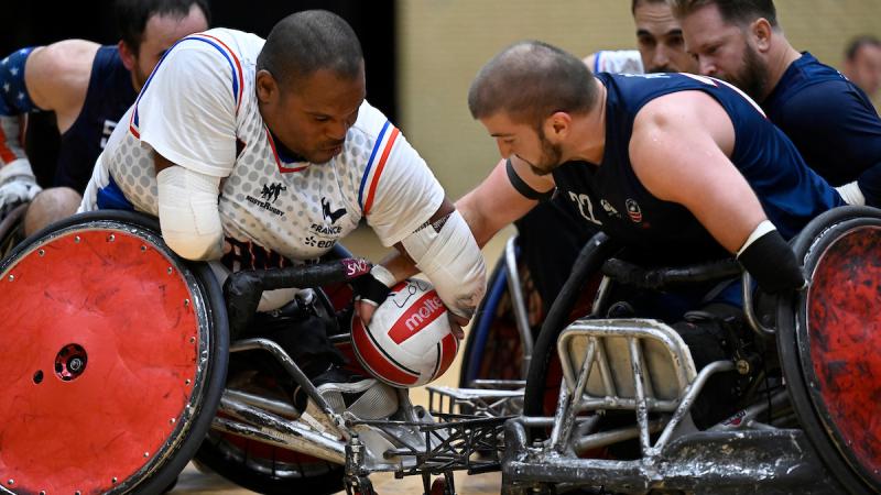 Two wheelchair rugby players reach for a ball