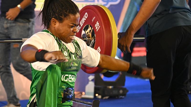 A woman in a green jersey and a white T-Shirt raises her arms and makes a strong gesture with her face.