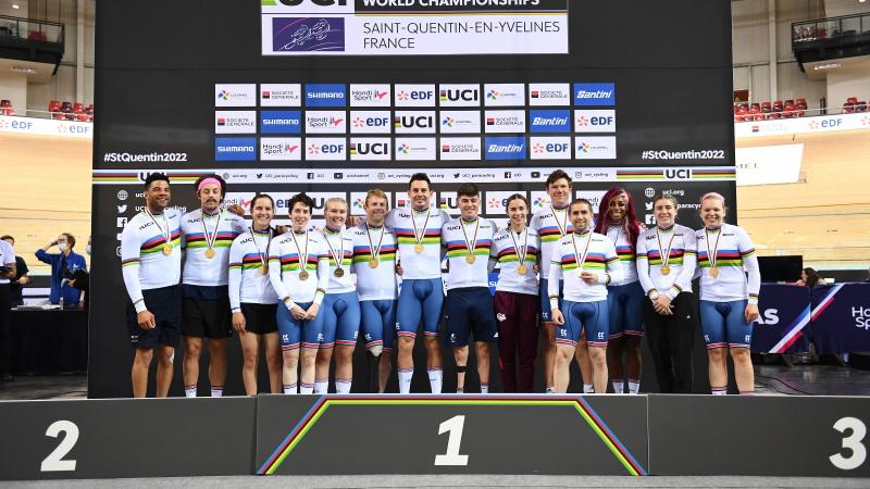 Fourteen British Para cyclists, all with medals, pose for a group picture on the podium.