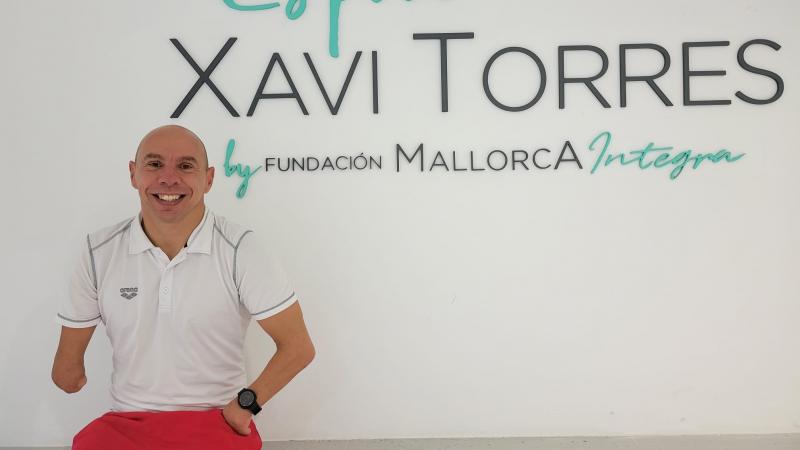 A male athlete smiles in front of the wall with the words "Espai Xavi Torres by Fundacion Mallorca Integra"