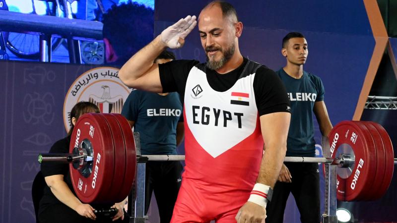 A man salutes with his right arm after lifting weights on a bench press.