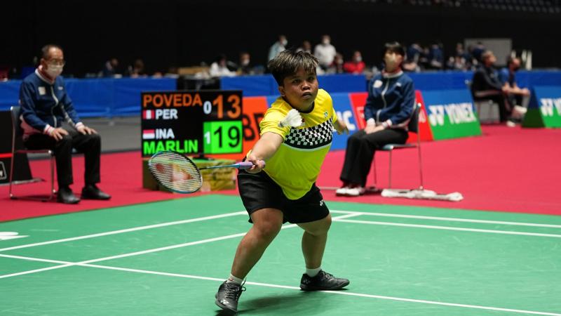 A female athlete holds a racket with her left hand and reaches out for the shuttle.