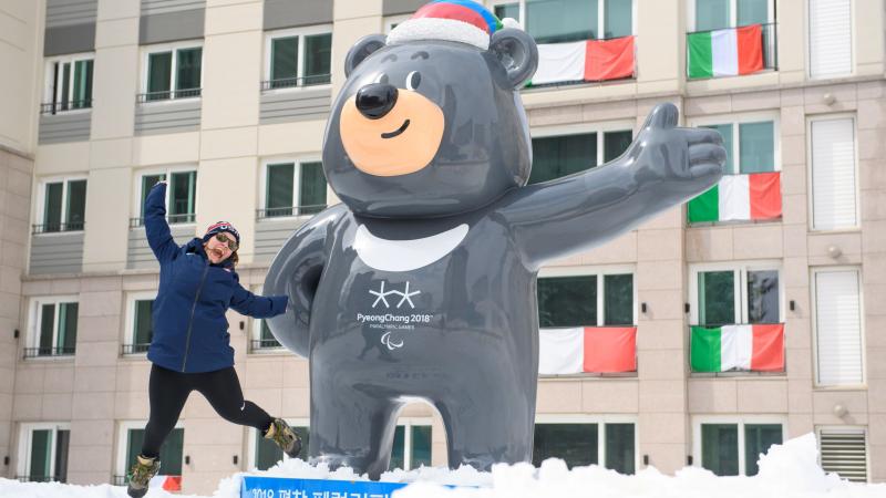 A woman jumps next to a mascot of the Pyeongchang 2018 Paralympic Games