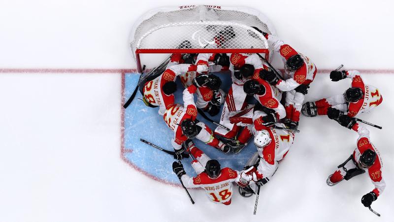 An aerial view of a Para ice hockey team celebrating in front of the goal on an ice rink