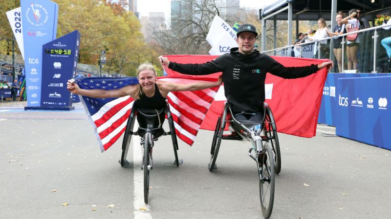 A female wheelchair racer with the USA flag and a male racer with the Swiss flag in front of a marathon finishing line
