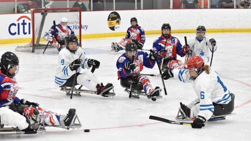 Seven female Para ice hockey players on ice in front of a goalie