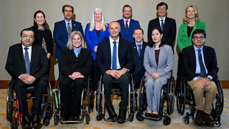 Twelve people in suits, five in the front row in wheelchairs, pose for a group photo.