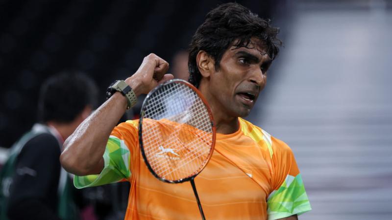 A male athlete pumps his right fist, while holding a badminton racket with the other hand