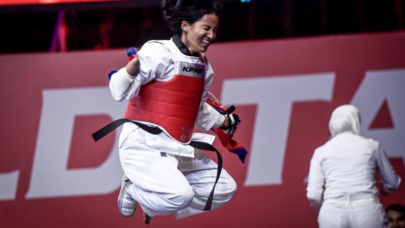 A female Para taekwondo athlete jumps with joy while holding a Nepalese flag after winning the final fight.