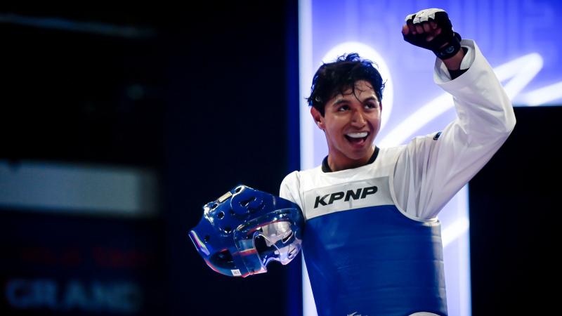 A male Para taekwondo athlete pumps his fist with his helmet off.