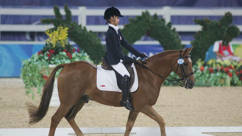 A female athlete rides a horse, walking calmly, during competition.