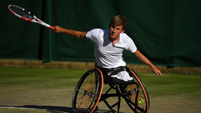 A male wheelchair tennis player extends his arms after returning the ball.