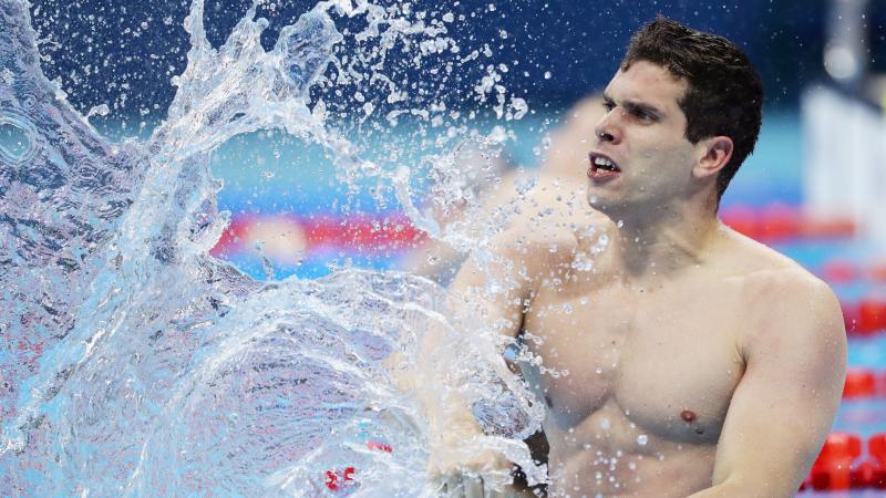 A male swimmer creates a big splash as he hits the water with his right fist after the finish of the race.