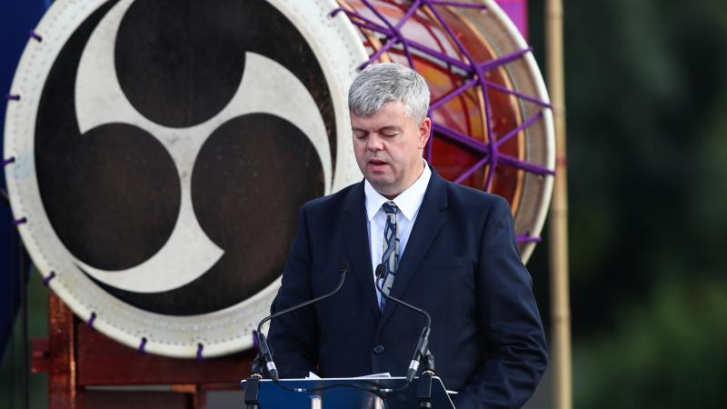 A man in a suit with a vision impairment speaks at a podium on a stage.