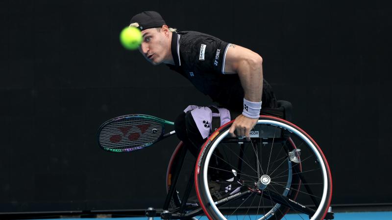 A male wheelchair tennis player eyes the ball with focus as he prepares to return it during a match.