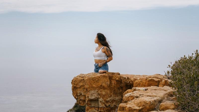 A young female without legs below the hips stands on a cliff looking out a large body of water.