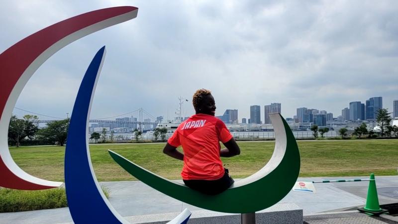 A female athlete wearing Japan's red uniform sits on the Three Agitos monument.